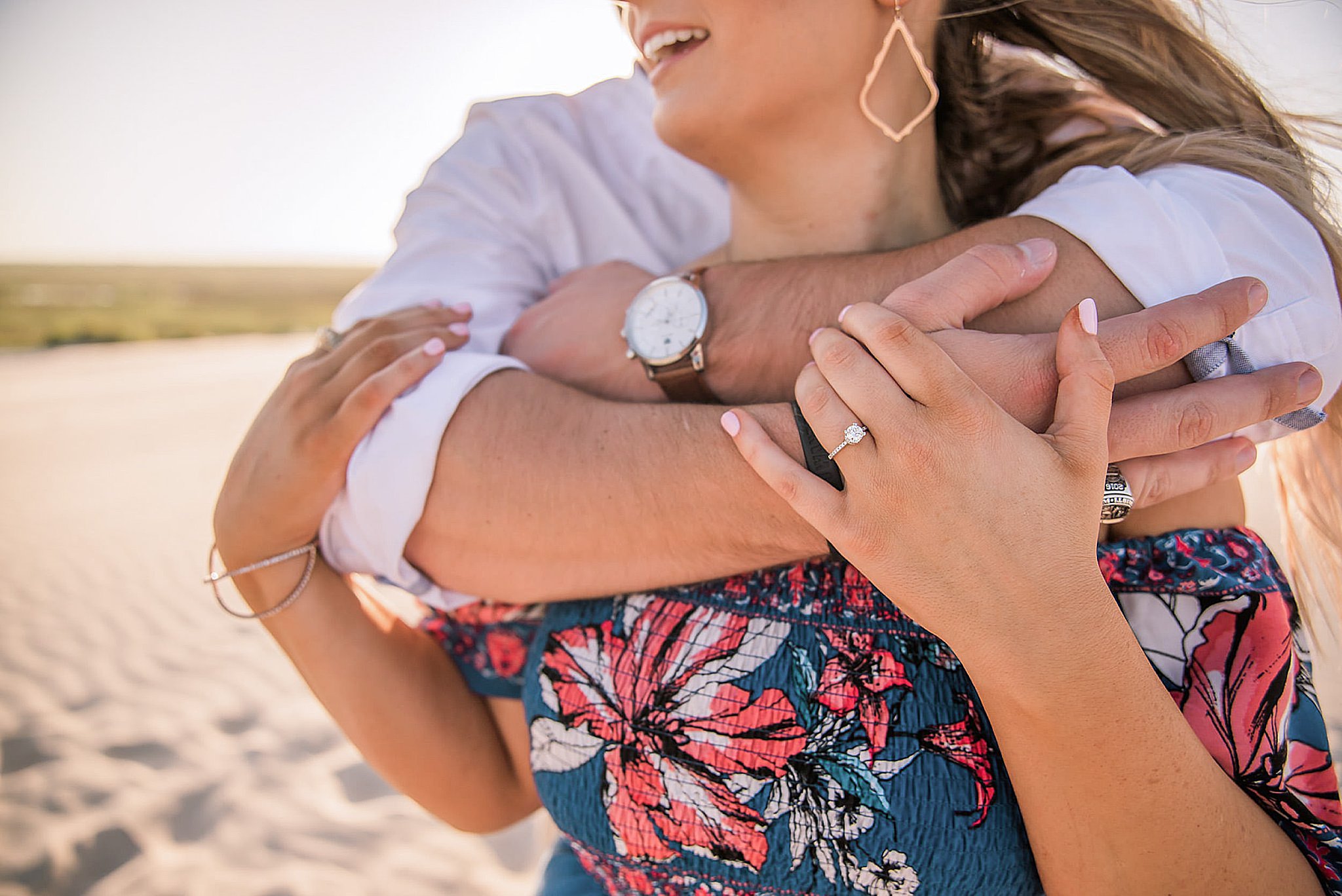 Woman in blue floral dress with mans arms wrapped around her shoulders during north padre island engagement.