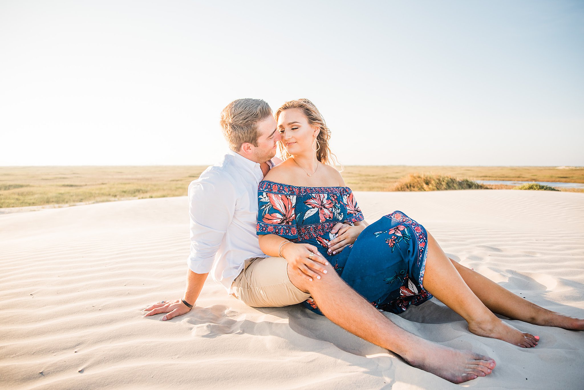 Couple laying together at the top of a sand dune. Couple is nose to nose during north padre island engagement.