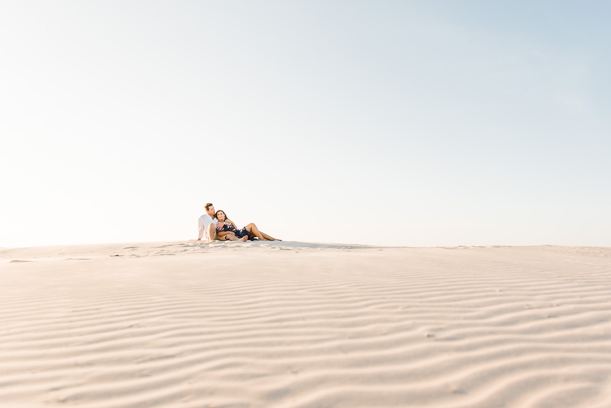 Couple laying together at the top of a sand dune during north padre island engagement.